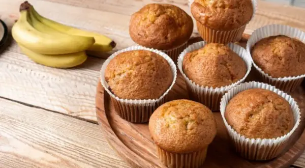 Puszyste babeczki bananowe, świeżo upieczone, kuszą swoim aromatem. Obok leży kiść dojrzałych bananów.