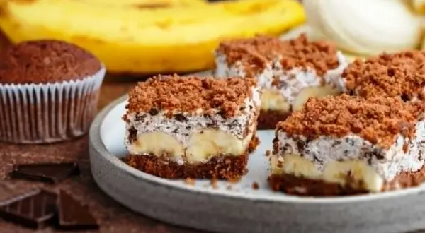 Słodki kopiec kreta z bananami, kremem i czekoladową posypką. Obok babeczka i kawałki czekolady.