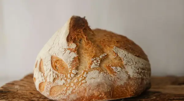 Chrupiący, złocisty zakwas pszenny z wyrazistym nacięciem i wzorem na skórce, ułożony na drewnianej desce.