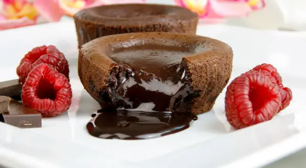 Płynny środek gorącego lava cake spływa na talerz, otoczony malinami i kawałkami czekolady.