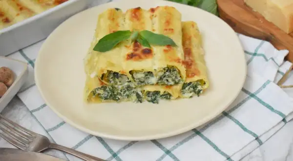 Pyszne cannelloni ze szpinakiem i serem, zapieczone pod beszamelem, ozdobione listkiem bazylii.