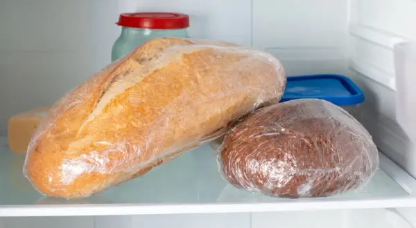Dwa bochenki chleba, jeden jasny, drugi ciemny, zawinięte w folię spożywczą, leżą na półce lodówki. To może być odpowiedź na pytanie, dlaczego chleb pleśnieje.