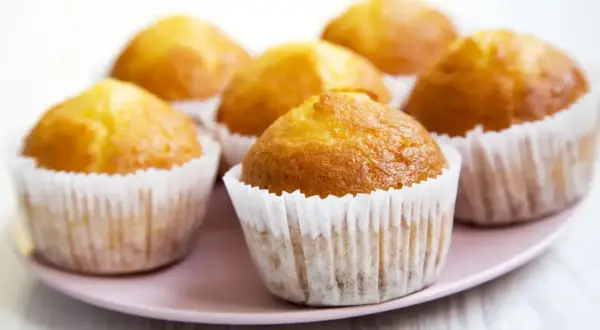 Sześć złotych muffinek w papierowych foremkach na różowej paterze. Idealne na szybki muffinki przepis.
