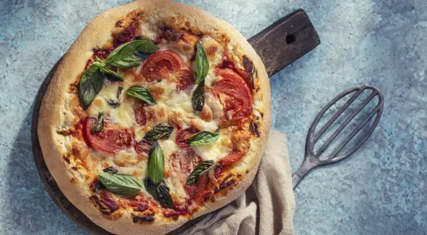 Pyszna pizza bez drożdży z pomidorami i bazylią, podana na drewnianej desce.