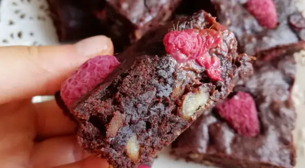 Pyszne brownie z malinami i orzechami, trzymane w dłoni.