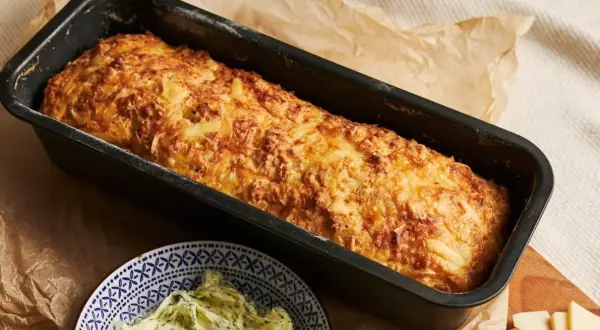 Złocista babka ziemniaczana w keksówce, obok miseczka z ziołowym masłem. Idealna na rodzinny obiad.