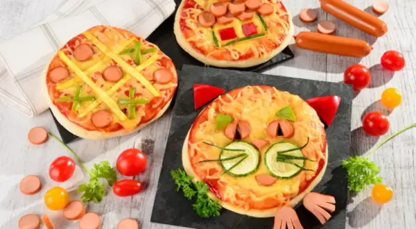 Wesołe pizza dla dzieci: jedna w kształcie kota, druga jak kółko i krzyżyk, trzecia z parówkami i papryką.