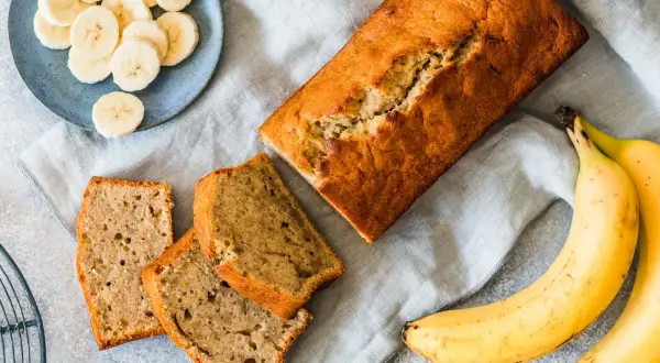 Chlebek bananowy, pokrojony w plastry, z bananami i plasterkami na talerzyku. Kwestia smaku, czy wolisz cały bochenek, czy kawałek.