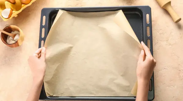 Dłonie układają papier do pieczenia na blasze. Zastanawiasz się, czym zastąpić papier do pieczenia? Oto praktyczne rozwiązanie!