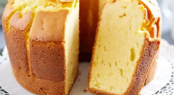 Puszysta babka pomarańczowa, zrumieniona na zewnątrz, z widocznym kawałkiem ciasta. Idealna na popołudniową herbatę.