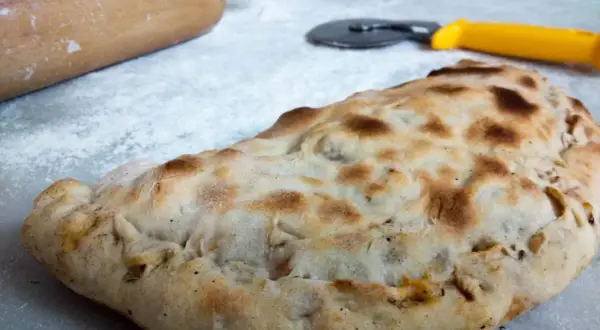 Złocisty calzone, gotowy do podania. Obok wałek i nóż do pizzy, jakby ktoś właśnie skończył przygotowywać ten pyszny przepis.