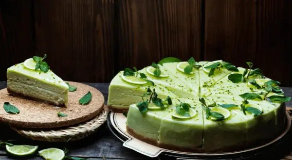 Zielony sernik pistacjowy, udekorowany plasterkami limonki i miętą, wygląda apetycznie.