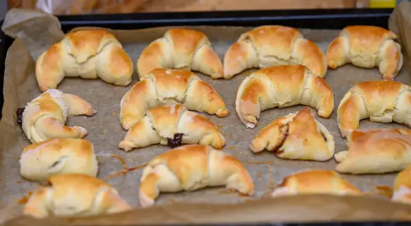 Szybkie rogaliki kruche, lekko zarumienione, ułożone na blasze wyłożonej papierem do pieczenia. Niektóre z nadzieniem.