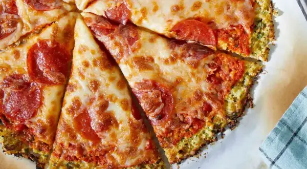 Pyszna pizza na spodzie z kalafiora z serem i pepperoni, pokrojona na kawałki.