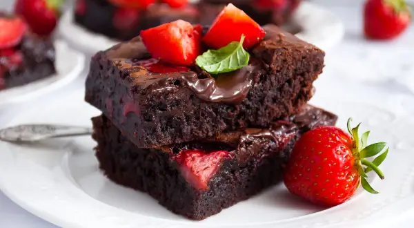 Pyszne brownie z truskawkami, polane czekoladą i ozdobione listkiem mięty. Idealne na deser!