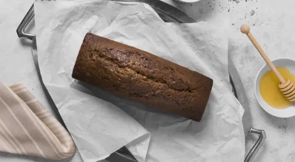 A pyszny, domowy chleb czekoladowy na tacy, obok miseczki z miodem i nasionami.