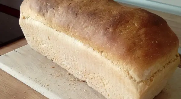 Puszysty chleb na suchych drożdżach, z chrupiącą skórką, leży na drewnianej desce. Idealny do kanapek.