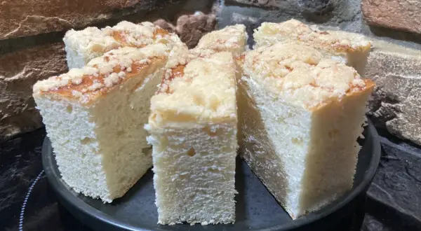 Puszyste ciasto drożdżowe z kruszonką, pokrojone na kawałki, prezentuje się apetycznie na czarnym talerzu.