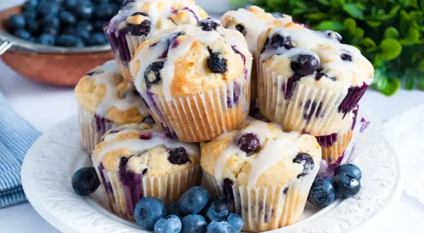 Stos pysznych muffinek z borówkami, polanych lukrem, ozdobionych świeżymi borówkami. Idealne na śniadanie lub deser.