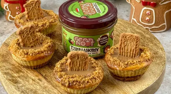 Urocze mini serniczki z kremem orzechowym i ciasteczkiem na wierzchu, obok słoiczek pasty z prażonych orzechów.