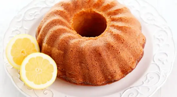 Puszysta babka cytrynowa na ozdobnym talerzu, z dwoma plasterkami cytryny obok. Idealna na popołudniową herbatkę.