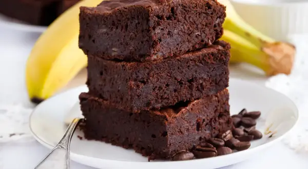 Stos puszystych brownie z bananami, ozdobiony ziarnami kawy, na talerzyku z łyżeczką.