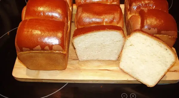 A fresh batch of chleb hokkaido, golden brown and fluffy, awaits. Two loaves are sliced, revealing their soft, airy crumb.