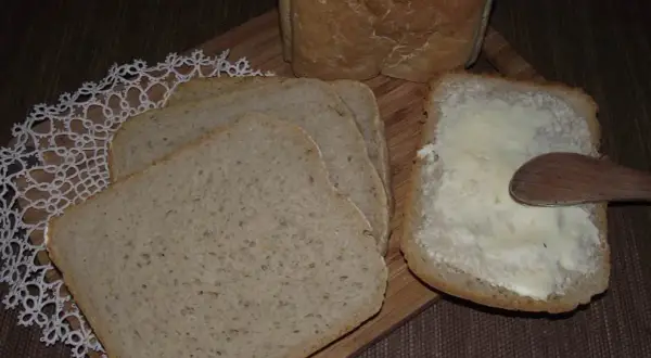 Chleb na zakwasie z maszyny, pokrojony w kromki, jedna posmarowana masłem.