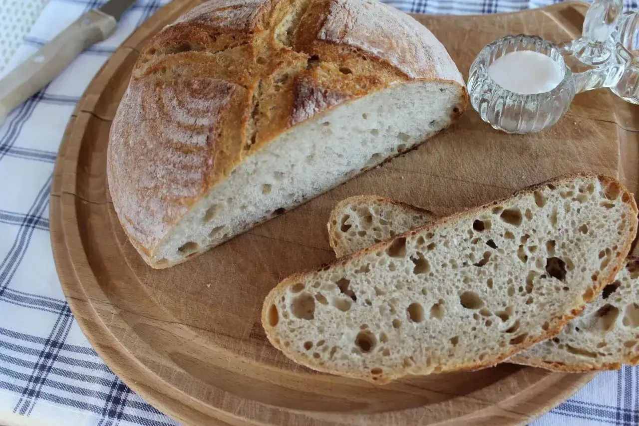 Chleb z mąki żytniej, pokrojony na desce, z solniczką i nożem w tle.