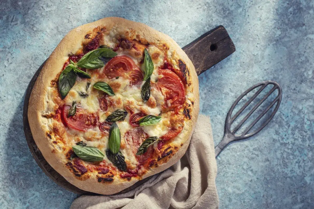 Pyszna pizza bez drożdży z pomidorami i bazylią, podana na drewnianej desce.