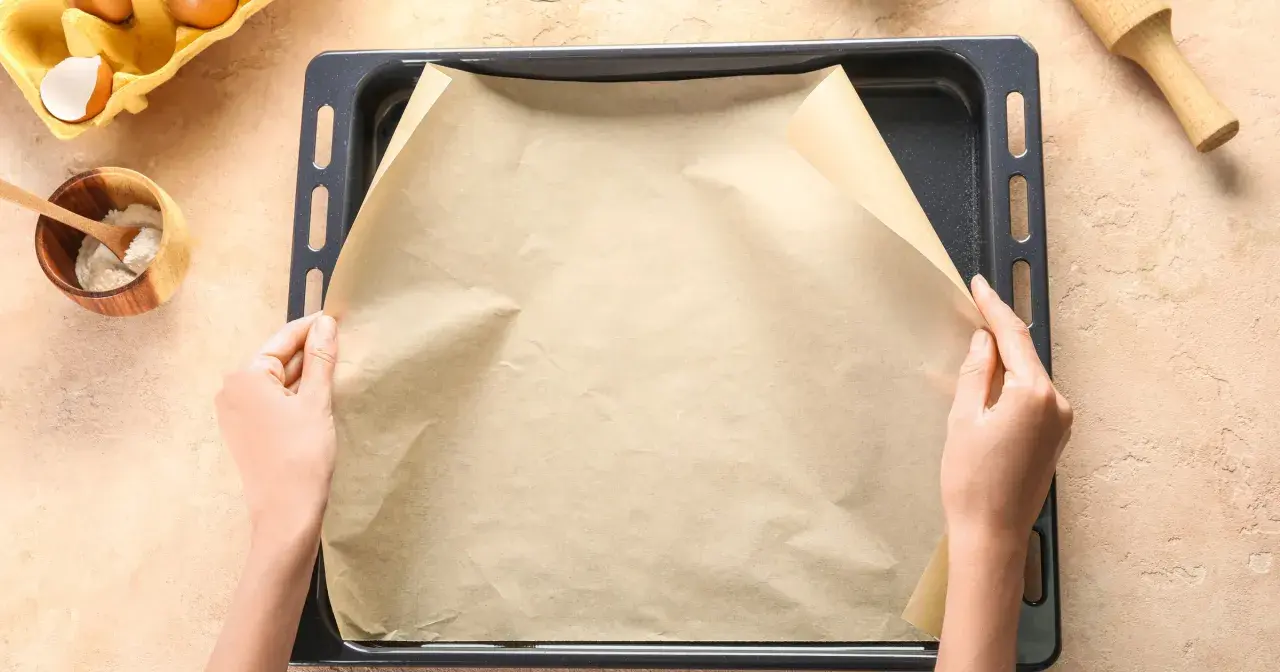 Dłonie układają papier do pieczenia na blasze. Zastanawiasz się, czym zastąpić papier do pieczenia? Oto praktyczne rozwiązanie!