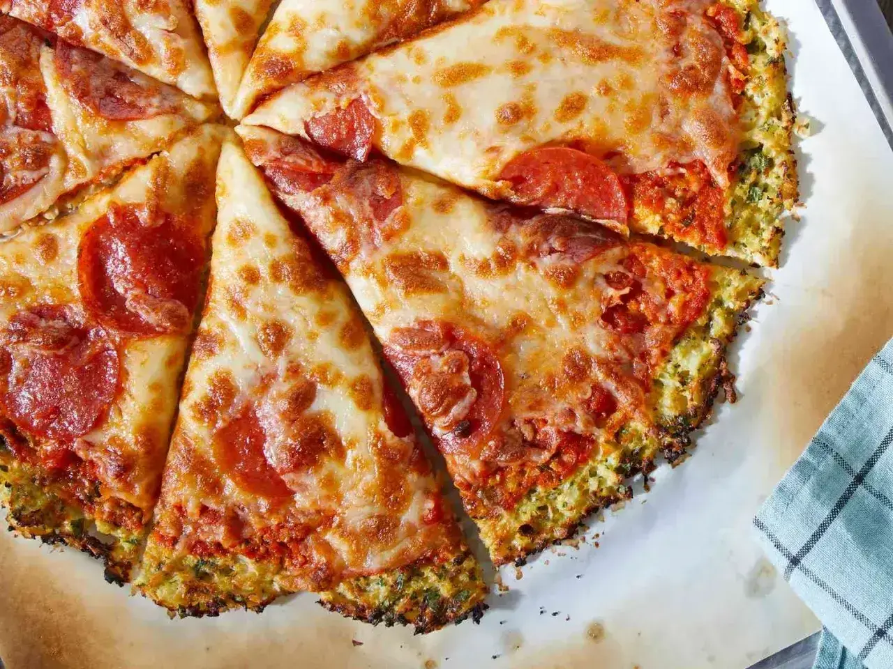 Pyszna pizza na spodzie z kalafiora z serem i pepperoni, pokrojona na kawałki.
