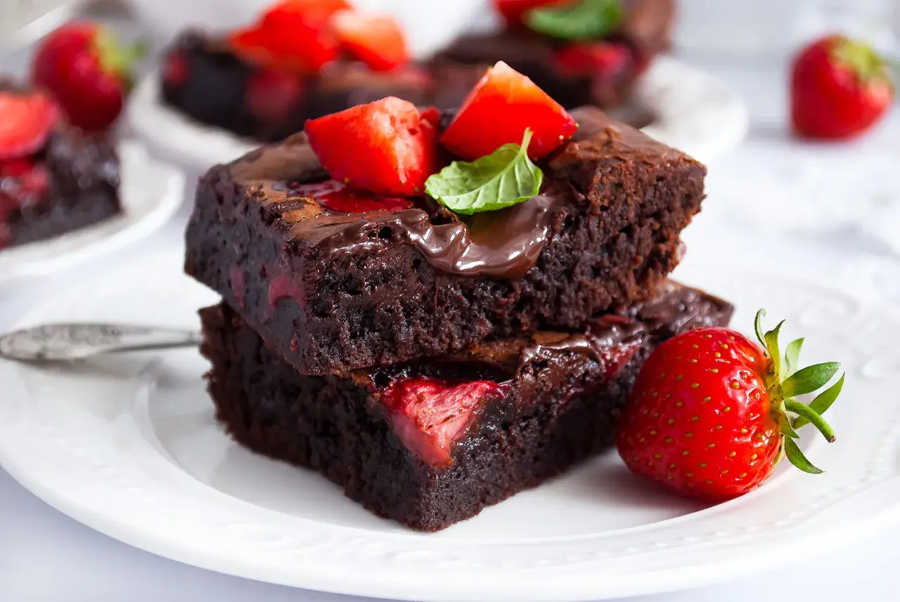 Pyszne brownie z truskawkami, polane czekoladą i ozdobione listkiem mięty. Idealne na deser!