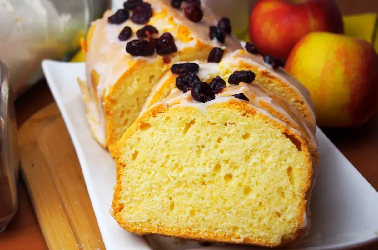 Najlepsza babka cytrynowa wilgotna na oleju, polana lukrem i posypana żurawiną. Obok jabłka.