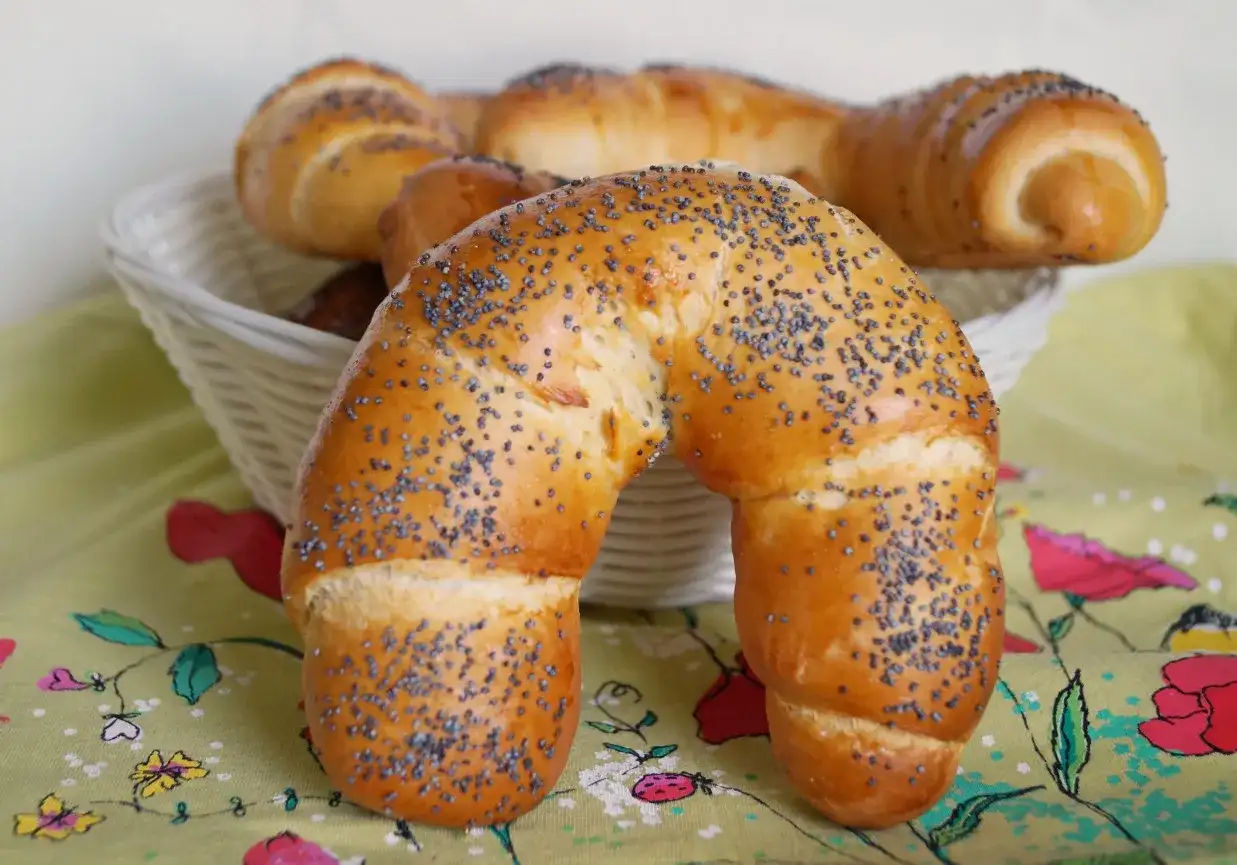 Złocisty rogal z makiem, świeżo upieczony, kusi swoim aromatem. W koszyku czekają kolejne pyszności.