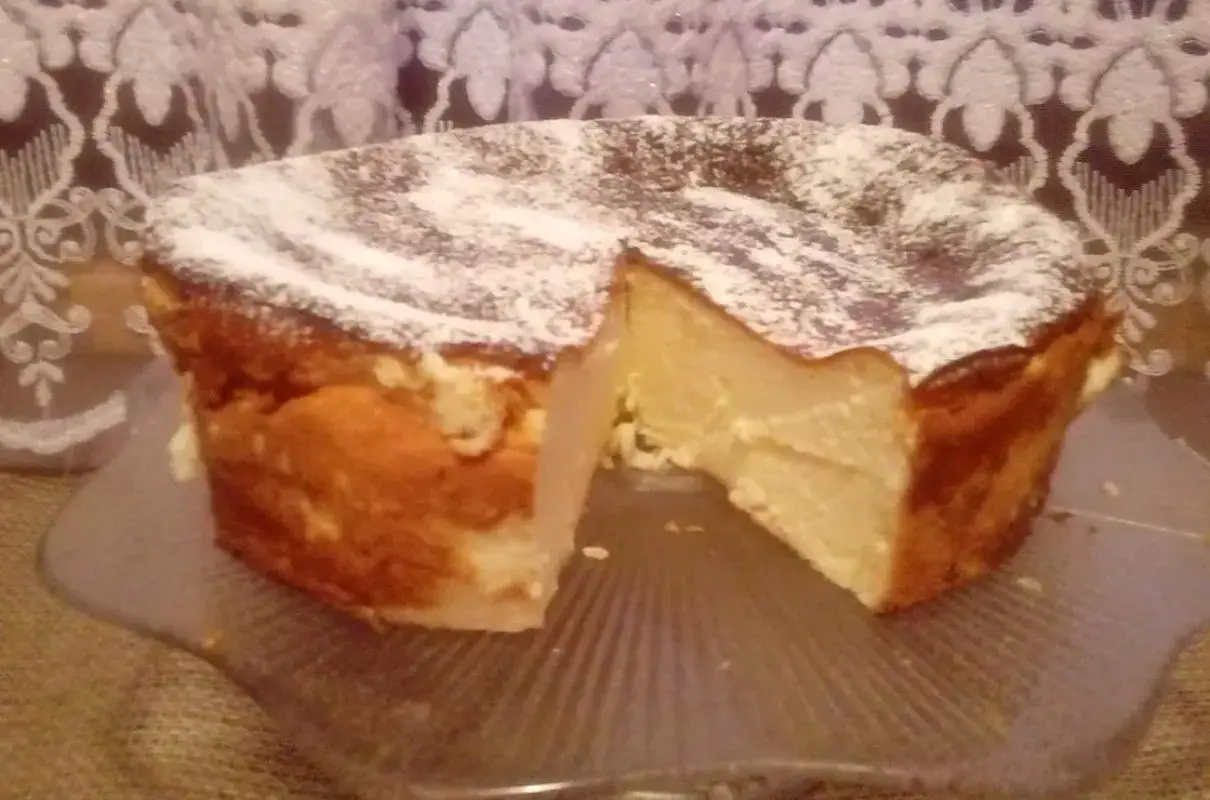 Puszysty sernik z mlekiem skondensowanym, posypany cukrem pudrem, prezentuje się apetycznie na szklanej paterze.