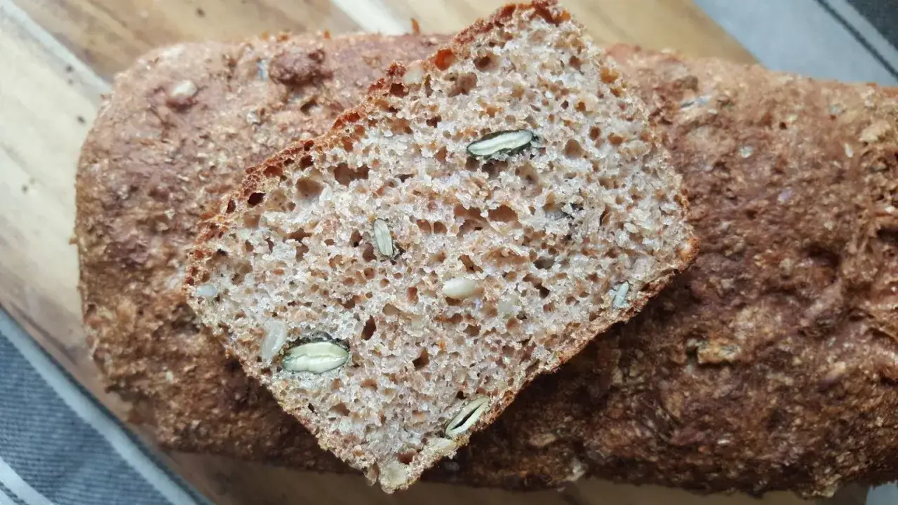 Kromka pysznego, domowego chleba razowego z pestkami dyni i słonecznika, ułożona na całym bochenku.