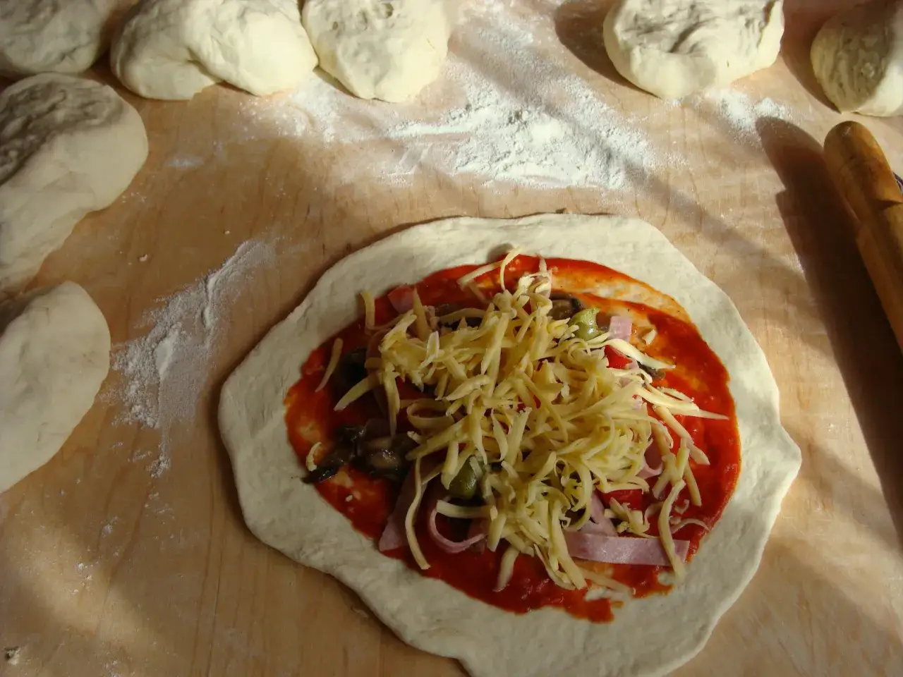 Przygotowania do domowego calzone: ciasto, sos pomidorowy, ser, szynka i warzywa. Przepis na pyszne calzone.