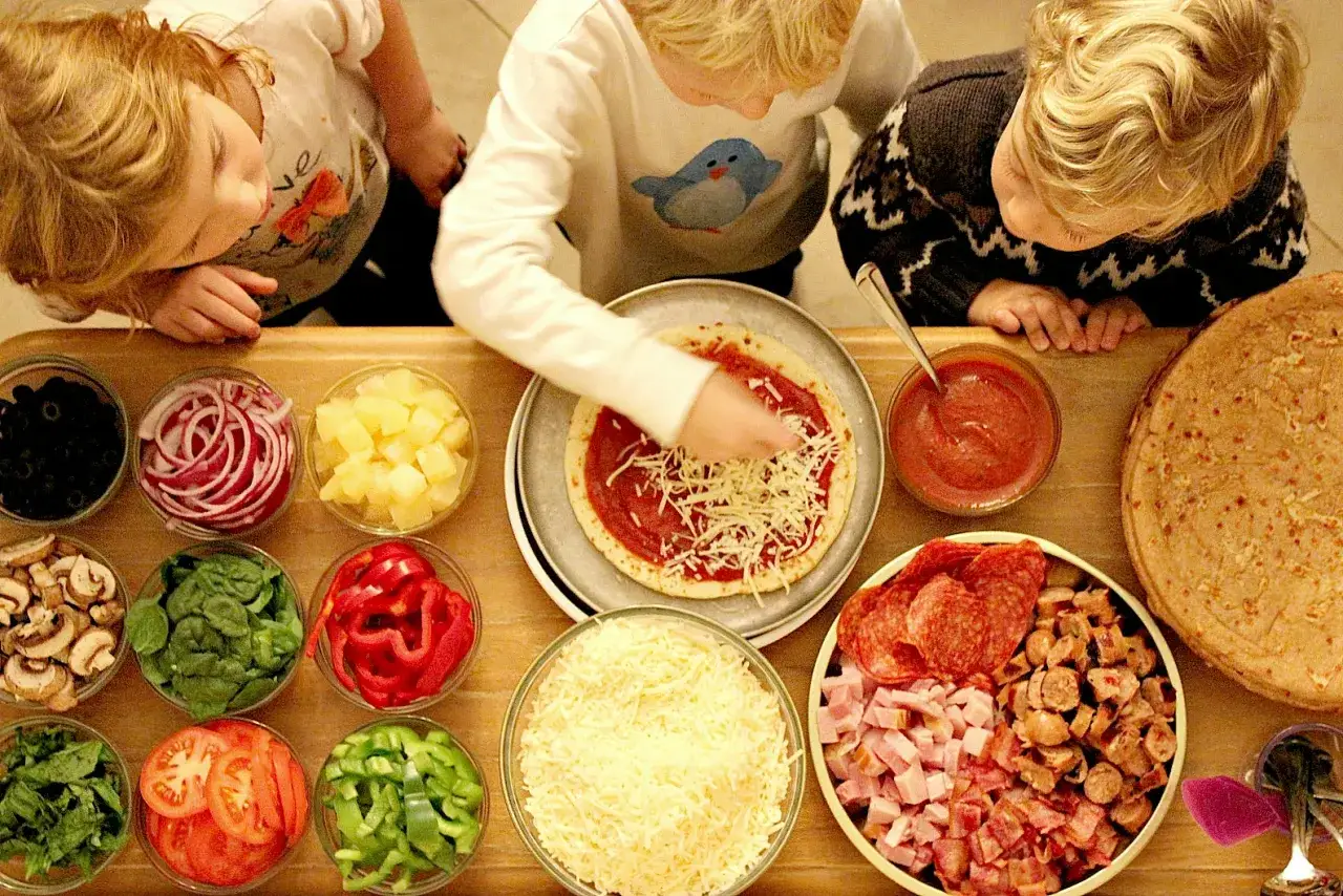 Dzieci tworzą własną pizzę, wybierając ulubione dodatki. Radość i kreatywność na talerzu!