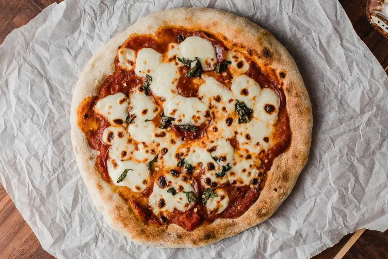 Pyszna pizza na zakwasie z ciągnącym się serem mozzarella i aromatycznymi listkami bazylii, podana na papierze do pieczenia.