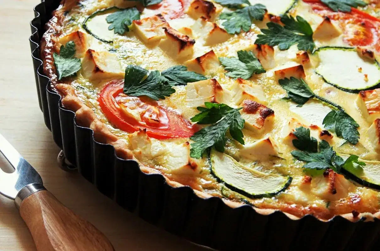 Pyszna tarta wytrawna z cukinią, pomidorami i serem feta, udekorowana natką pietruszki. Idealna na lekki obiad lub kolację.