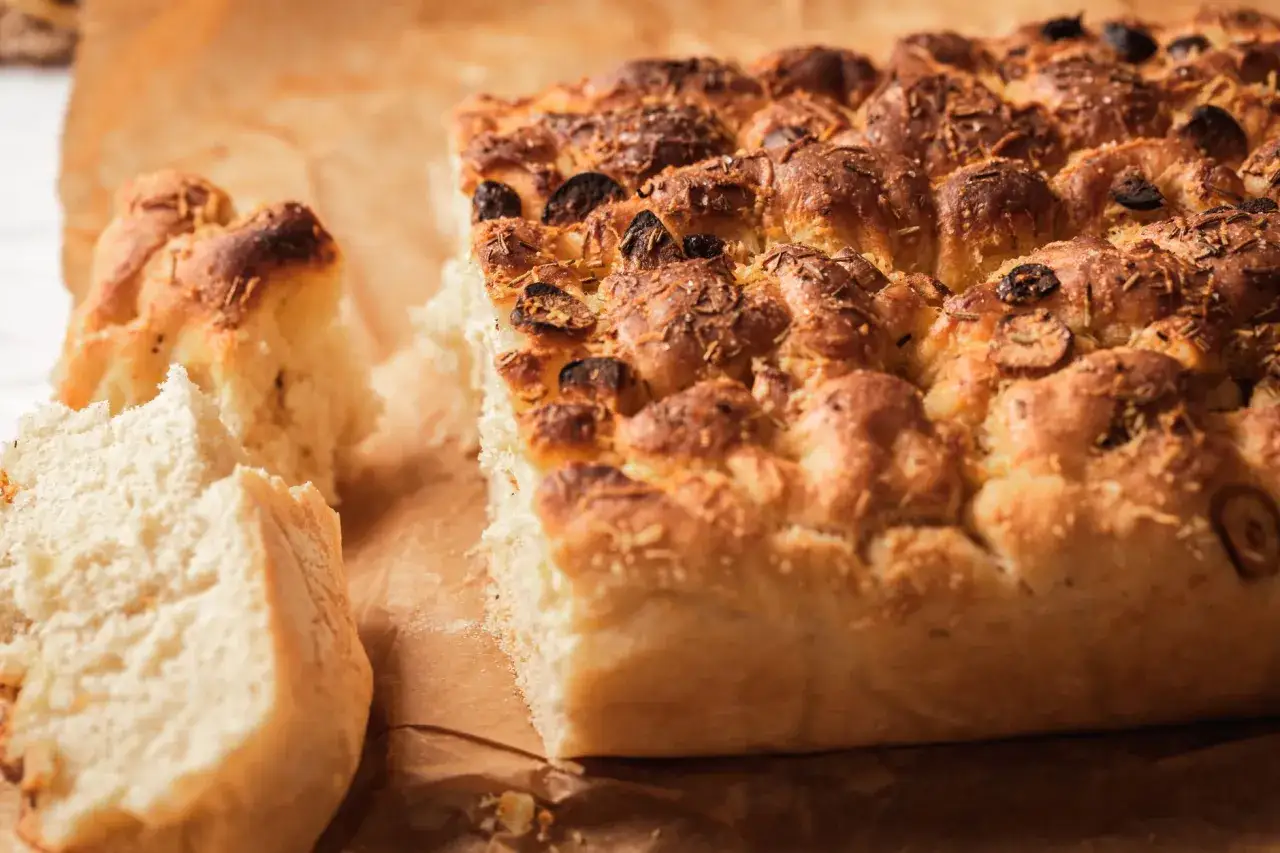 Chrupiąca focaccia z serem i ziołami, z widocznymi kawałkami oliwek, idealna na przekąskę.