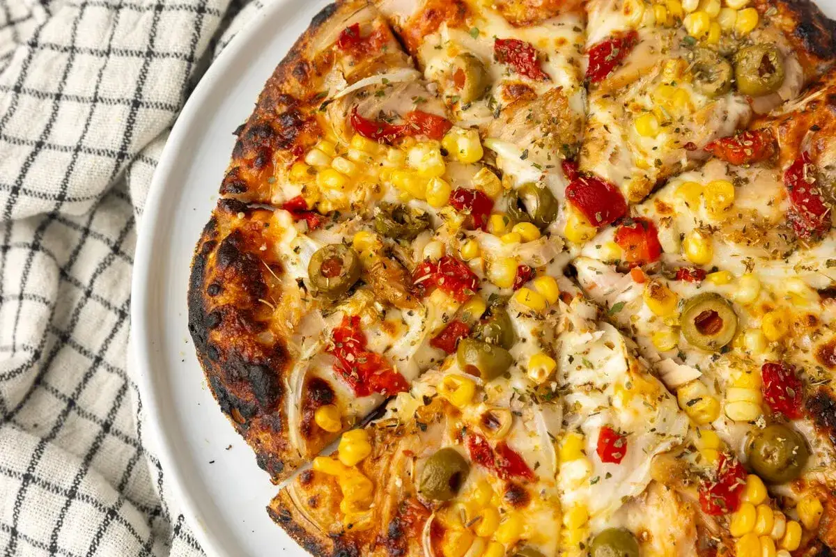 Apetyczna pizza z tuńczykiem, kukurydzą, oliwkami i papryką, z chrupiącym, lekko przypieczonym brzegiem.