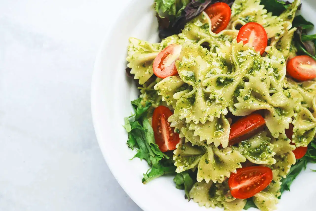 Makaron farfalle w sosie pesto bazyliowym z pomidorkami koktajlowymi i świeżą sałatą.