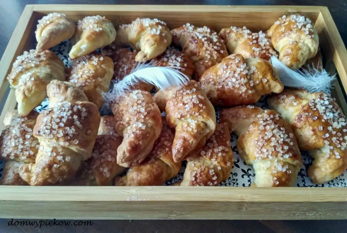 Złociste croissanty z czekoladą, posypane cukrem, kuszą swoim wyglądem. Puszyste piórka dodają im uroku.