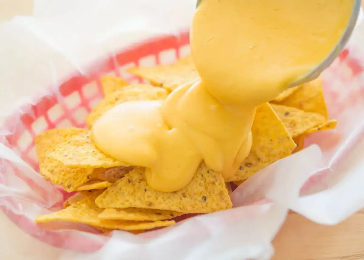 Chrupiące nachos w czerwonym koszyku, polane obficie kremowym, gorącym sosem serowym. Idealna przekąska na imprezę.