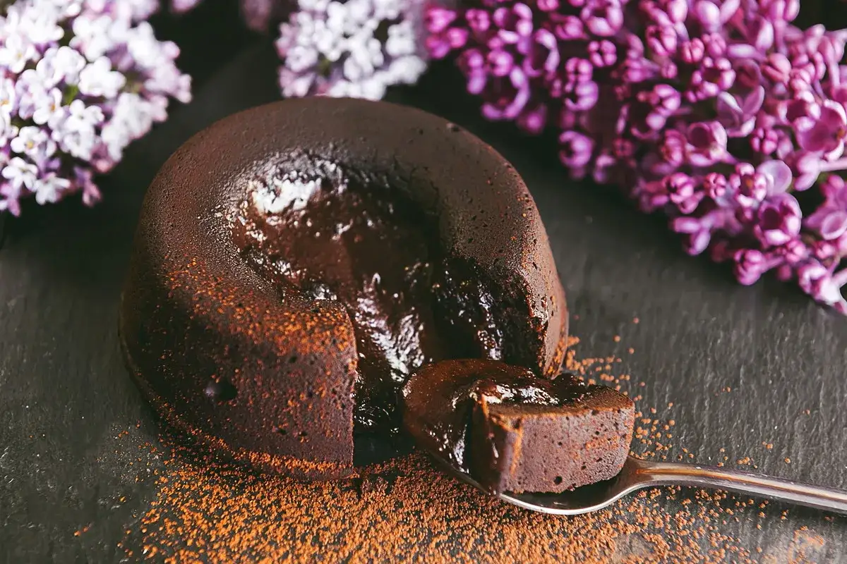 Czekoladowy lava cake z płynnym środkiem, posypany kakao, obok fioletowych bzów.