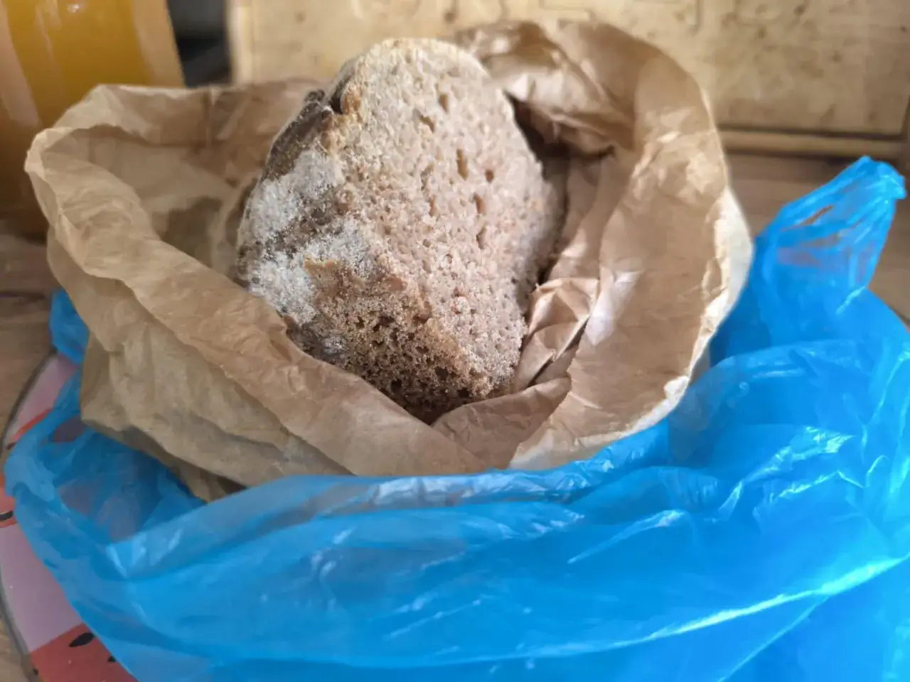 Kawałek chleba w papierowej torbie, otoczony niebieską folią. Zastanawiasz się, czy chleb można trzymać w lodówce?