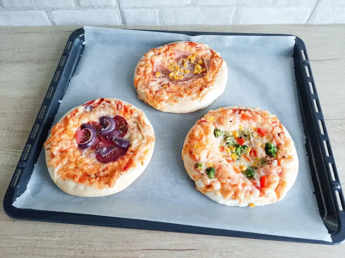 Gotowe pizzerinki na blasze, z serem i różnymi dodatkami: cebulą, kukurydzą, brokułami. Idealne do wypróbowania pizzerinki przepis!