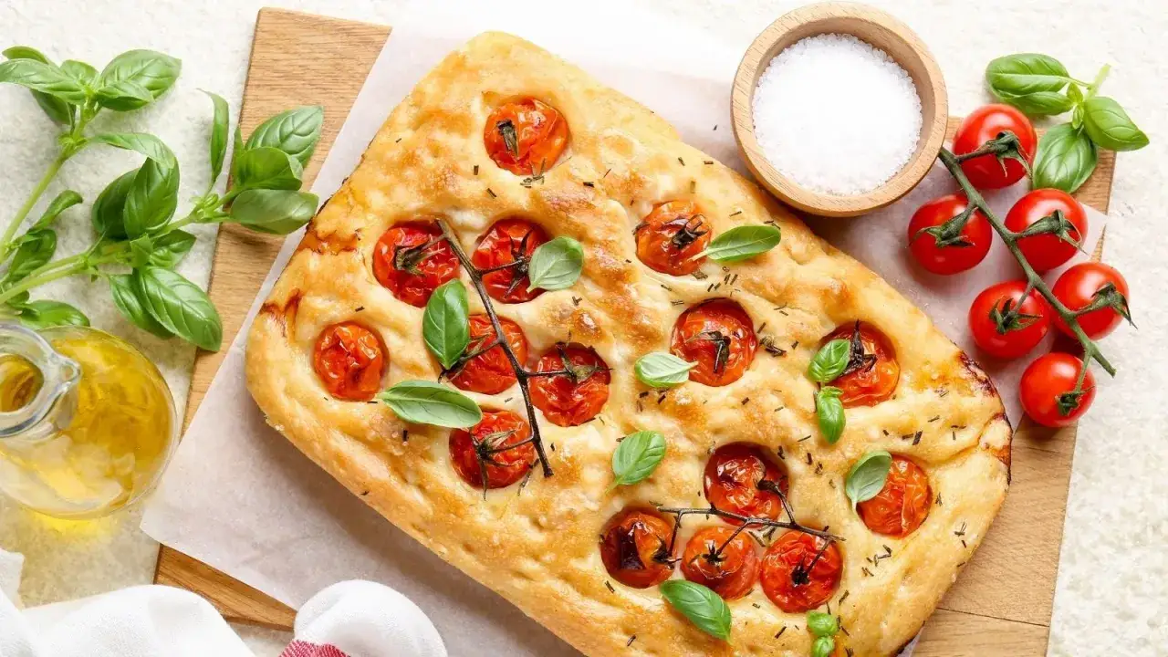 Pyszna focaccia z pomidorkami koktajlowymi i bazylią, obok oliwa, sól i świeże pomidory. Idealna na letnie popołudnie.